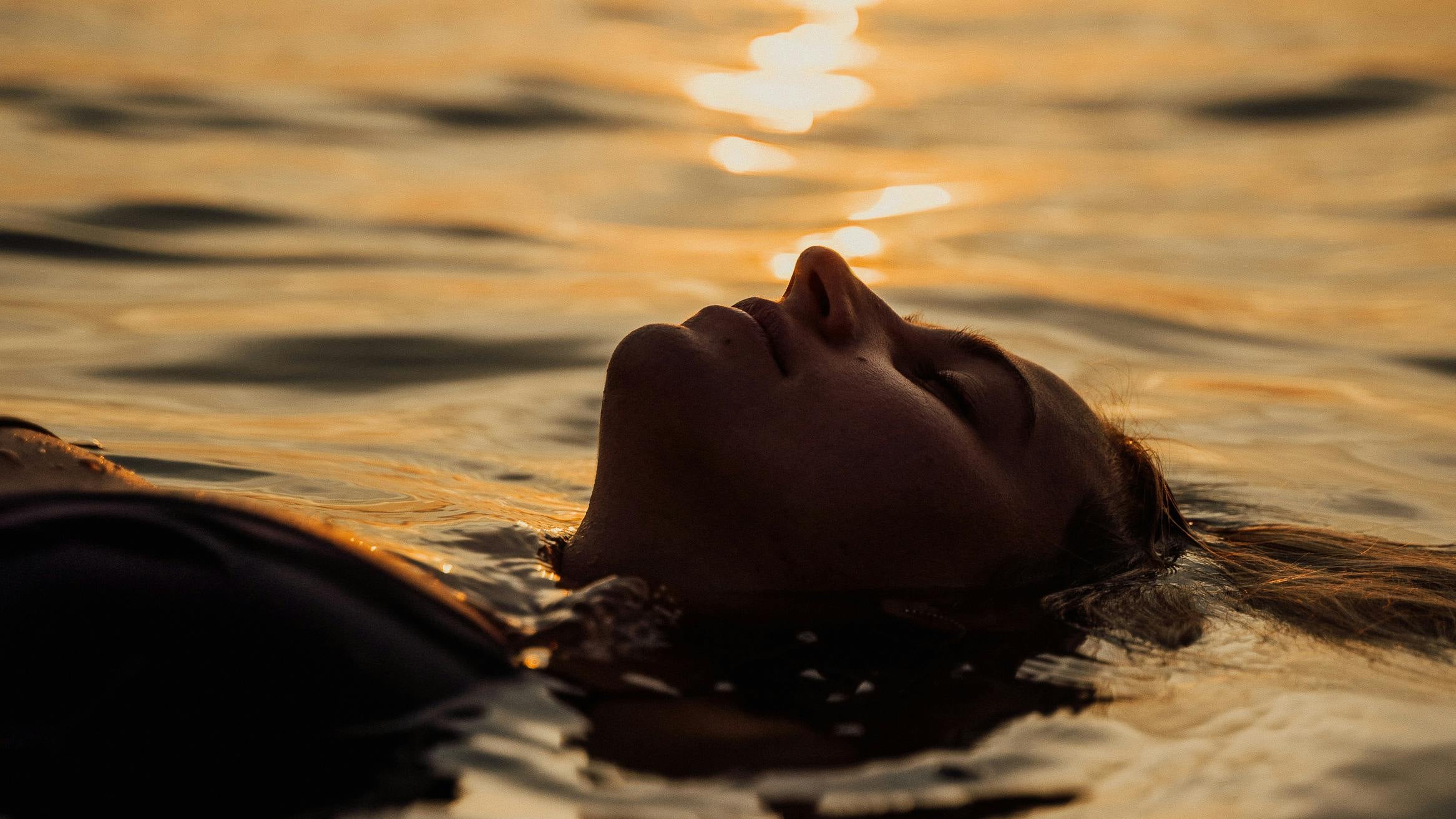 femme qui se beigne dans l'eau au soleil couchant.